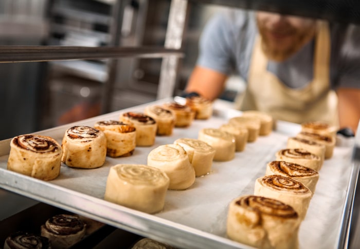 un homme glisse un plateau de roulés dans une échelle patissière